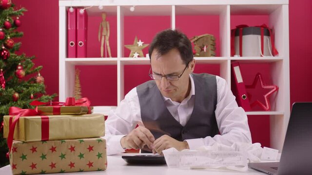 Christmas suicides ironic concept. worried 40s businessman counts expenses on calculator and desperately looks at hangmans noose of red tinsel falling in frame. Festive depression, holiday bankruptcy