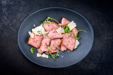 Modern Style traditionelles Roastbeef als kalte Platte Aufschnitt mit Rucola Salat und Parmesan Käse angeboten als Draufsicht in einem Design Teller
