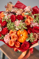 Red and orange flowers with pumpkin. Autumn bouquet of mixed flowers in glass vase on wooden table. The work of the florist at a flower shop. Fresh cut flower.