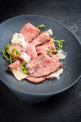 Modern style traditional lunch meat with sliced cold cuts roast beef with rocket salad and parmesan cheese offered as close-up in a modern design plate