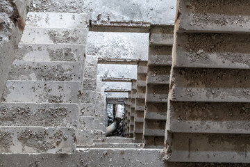 Dusty concrete staircase inside abandoned ruined building. Looking down perspective tunnel weathered multistorey house
