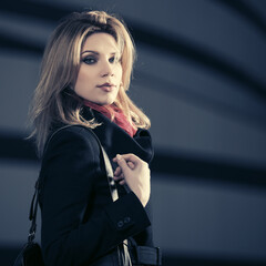 Fototapeta na wymiar Fashion blonde woman in black coat with leather handbag