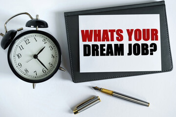 On the table there is a clock, a pen, a notebook and a card on which the text is written - WHATS YOUR DREAM JOB