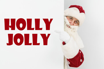 Santa Claus points his fingers at the board with the text - HOLLY JOLLY