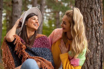 Fototapeta premium Two beautiful women are sitting, talking and smiling in the forest-park