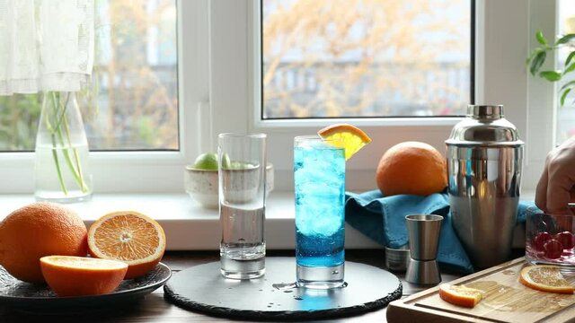 Real woman preparing a blue gin tonic cocktail with ice a mix of alcohol near the window on the table near window in the sunny falltime