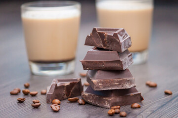 Pieces of dark chocolate, coffee beans and cups of cocoa or coffee with milk on wooden background.