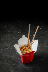 Udon noodles with fried chicken and vegetables in the cardboard box with wooden chopsticks