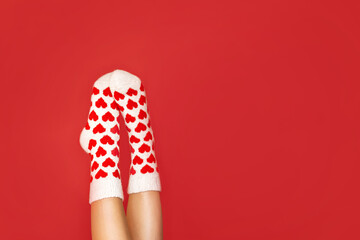 close-up of women's legs in warm socks with a heart print in a flirty pose on a red background with...