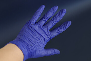 Rubber blue medical gloves on a female kavkazian hand on a dark background. Hand protection