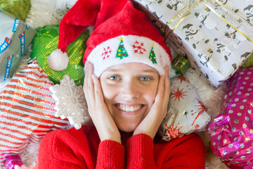 Christmas holidays excitement! Cheerful young woman surrounded by many Xmas presents wearing red hat.