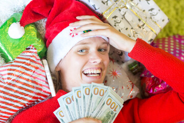 Joyful woman holding cash money next to Christmas gifts and wearing Santa hat.