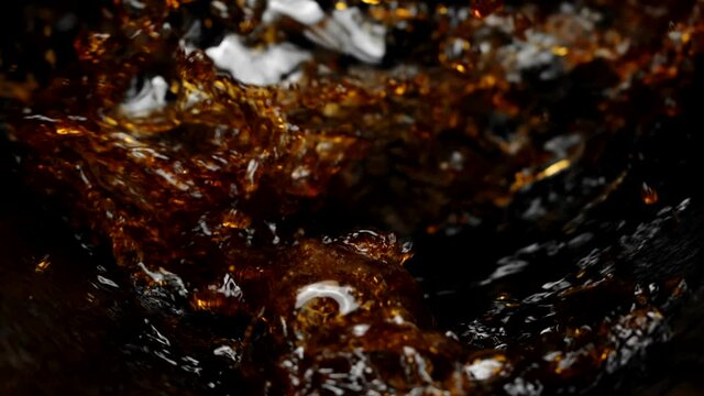 Dark sparkling liquid pouring splashing in slow motion on black background, drinks concept. Dark soda, dark beer, kvass, lager, black Ipa, brown Ale, Stout, Porter, Dunkel, Bock, Dunkelweizen
