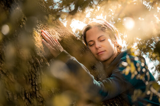 Close portrait of woman hugging the trunk of an old oak tree
