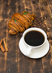 Fresh croissant and a cup of coffee on a wooden background.