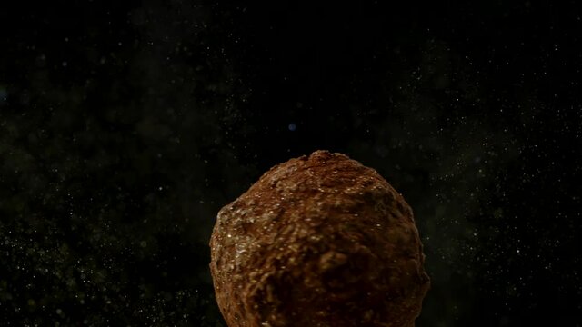 Macro shot of chocolate candy traditional french truffle spinning in golden luster shiny glitter dust, close-up, slow motion, isolated black background. Homemade delicious festive xmas sweets