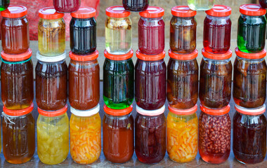 Different jams and pickles made from fruits and vegetables in glass bottles.