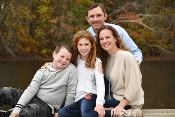 Fototapeta premium Autumn family portrait by the lake with mom, dad, son and daughter. 