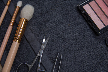 Various cosmetic products on a dark background.Makeup brushes, face shadows in different colors, scissors and chips.
