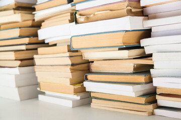 Background from tall stacks of different old and new books standing on a white table in sunny day.  Old books arranged in stacks. Books are not aligned. Selective focus.