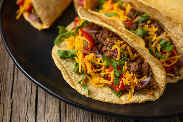 Close-up view of tasty mexican tacos with meat on black round plate on rustic wooden table. Traditional mexican cuisine.