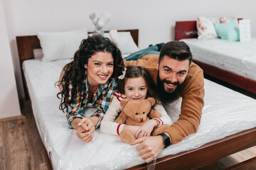 Young happy family buying new bed and mattress in big furniture store