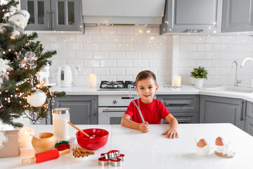 Boy sitting at the decorated Christmas table with a whisk in hand