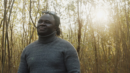 Naklejka premium Young african man walkling through the woods looking. Sunrays coming through trees. High quality photo