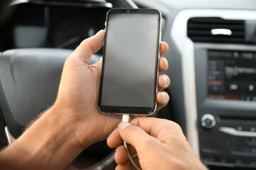 Man connecting charging cable to smartphone in car, closeup