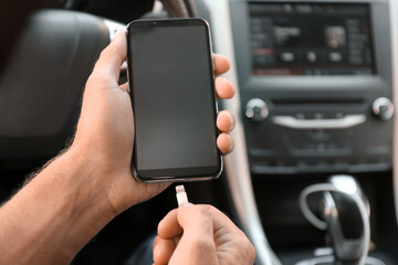 Man connecting charging cable to smartphone in car, closeup