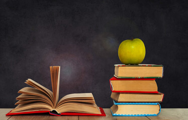 Open book textbook, pile of books and green apple on a wooden desk on the background of a green school chalkboard. Back to school distance home education.Quarantine concept of stay home