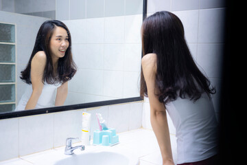 An Asian woman smiling to herself in front of a mirror in the bathroom, a bright new morning.