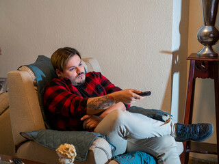 Obraz premium Hombre aburrido viendo la televisión en casa por el confinamiento y el toque de queda