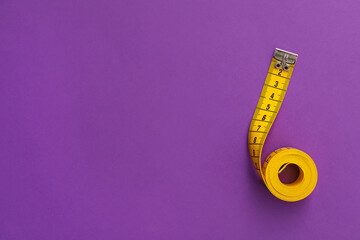 Yellow measuring tape on purple background, top view. Space for text