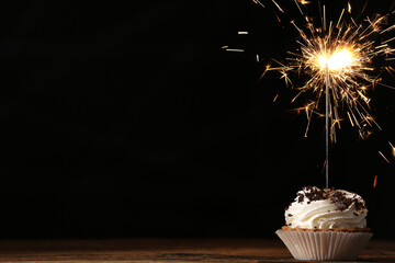 Delicious dessert with burning sparkler on wooden table against dark background, space for text