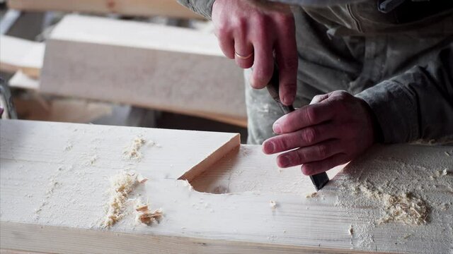 An unidintified carpenter is carefully working with chisel in his workshop