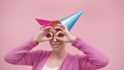 Crazy middle aged woman with 2 party hats and fingers forming glasses over her eyes isolated on...
