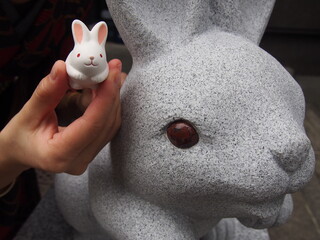 A cute little white rabbit statue and a large stone statue at Okazaki Shrine, Kyoto, Japan