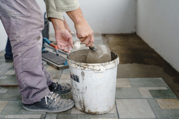 Close up on bucket with adhesive construction glue cement and unknown craftsmen holding tool in hand preparing material for ceramic tiles