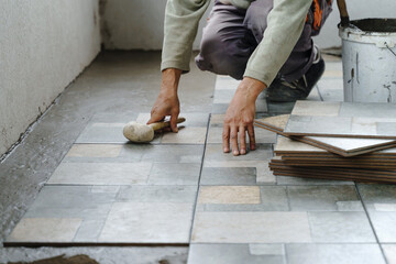 Close up on hands of unknown senior man craftsman using hammer to adjust and lay ceramic tiles on the balcony or terrace over adhesive cement in day - construction industry concept copy space