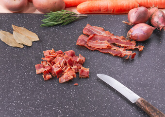 set of ingredients for the soup.

Step 5. Diced smoked bacon on a black board, with rosemary and...