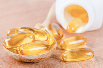 Fish oil capsules in wooden spoon with bottle.