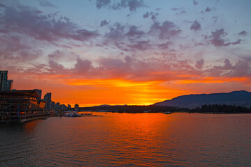 Spectacular sunset over Vancouver city harbor in Brithish Columbia, Canada. Scenic landscape litten by sunset with mountains chain at horison.