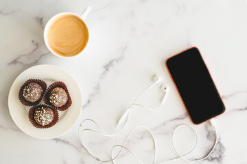 Coffee time. Cup of coffee, chocolate candy, cellphone, headphone close up on marble background, flat lay, copy space.