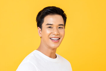 Close up portrait of happy young handsome Asian man cheerfully smiling and looking at camera in isolated studio yellow background