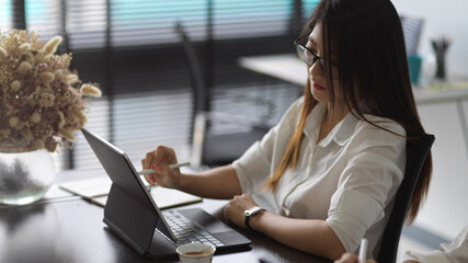 Female working with digital tablet with stylus and keyboard on worktable
