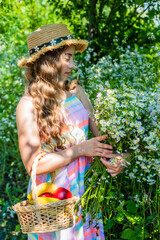 Small baby girl with long wavy hair in sun hat pick fruit and flowers in summer garden, farm