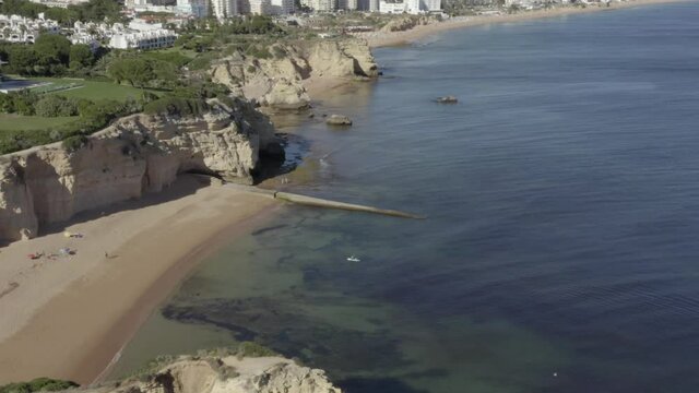 Flying over two people paddle boarding on an incredible tropical beach surrounded by beautiful oceanic cliffs, drone aerial