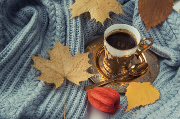 Coffee cup, autumn leaves and grey knitted sweater.