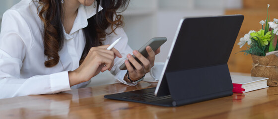 Female office worker using her smartphone while working her project with tablet